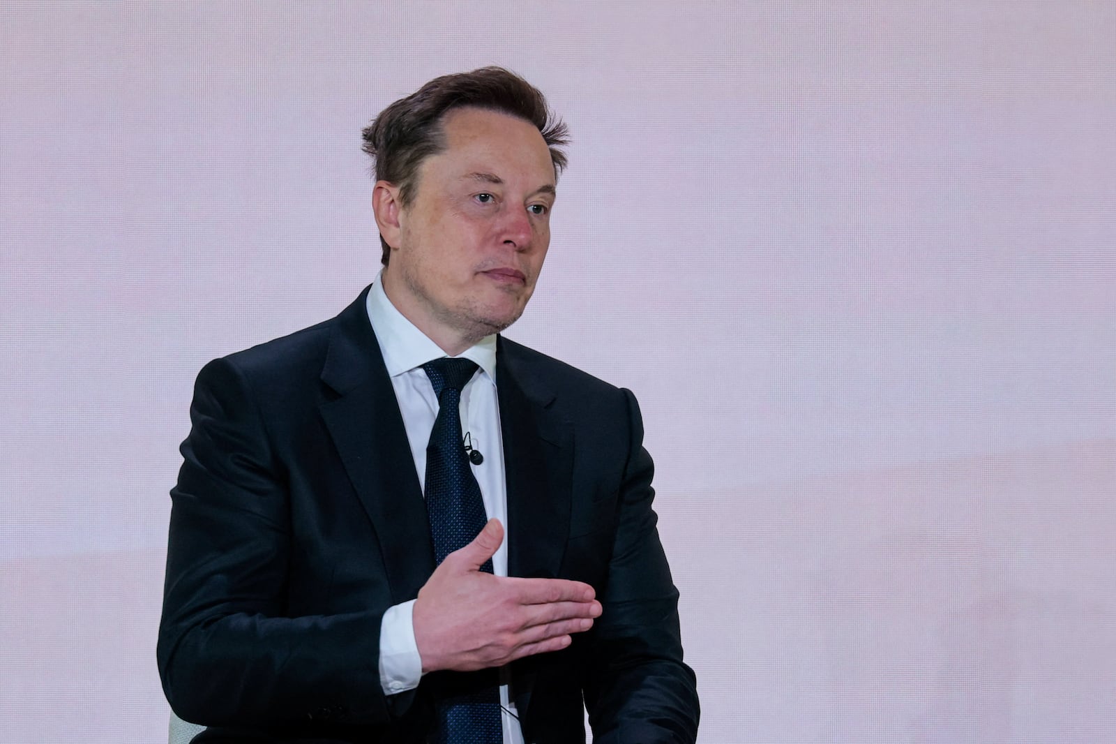 Elon Musk veste terno preto diante de parede branca