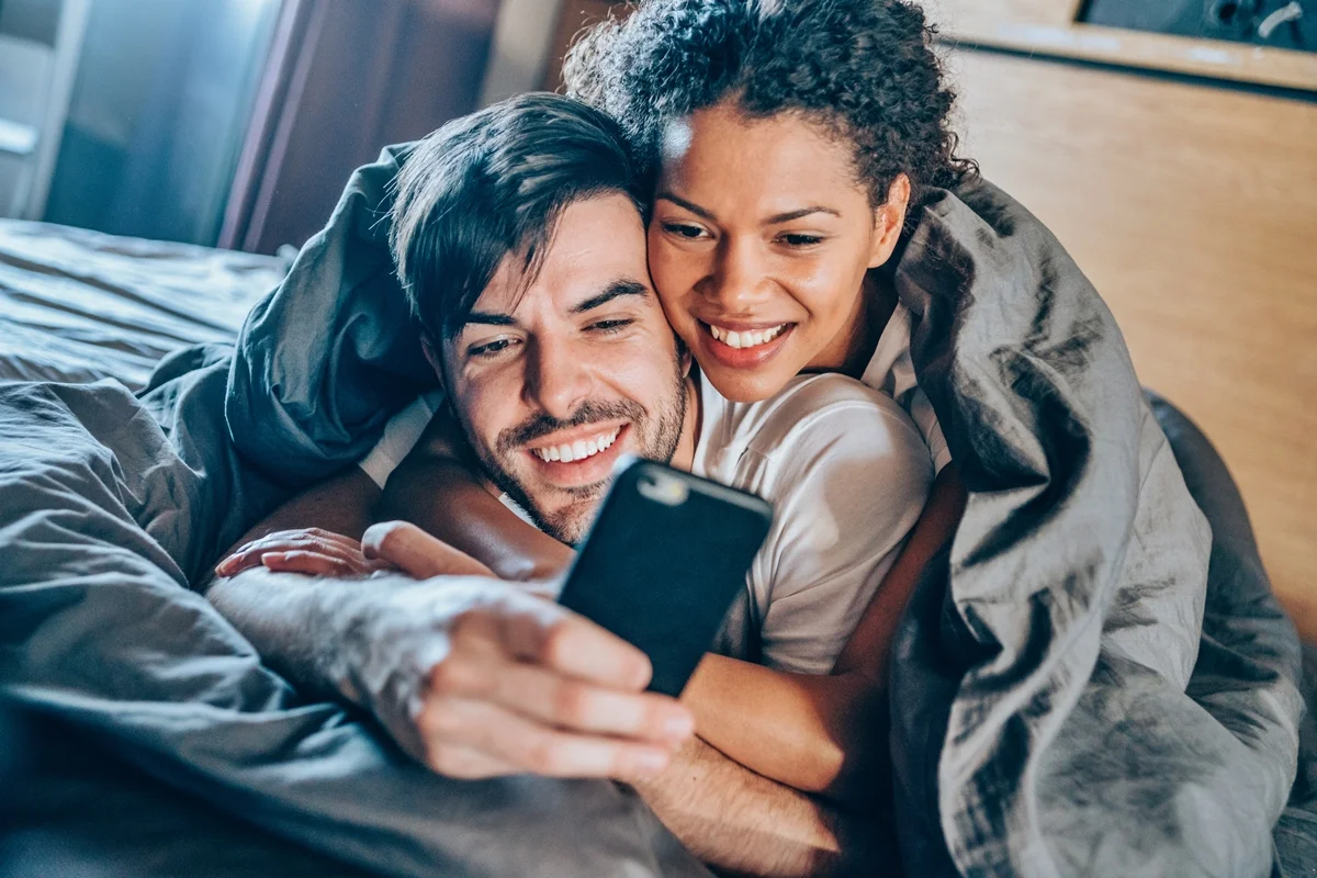 Casal deitado na cama enquanto mexem no celular