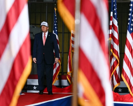 Donald Trump stands on a red carpet between US flags