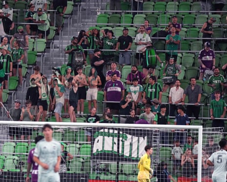 Austin FC fans stand and cheer in stadium stands behind a goal net
